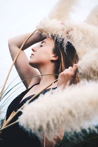 Side view of young woman holding cattail while standing outdoors