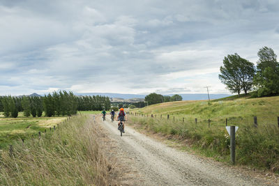 Rear view of man walking on road amidst field against sky