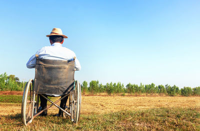 Rear view of man sitting on wheelchair against sky