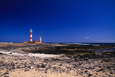 Lighthouse on beach by sea against sky