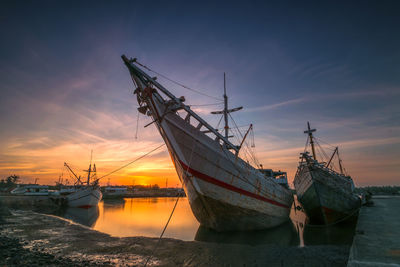 Sailboats moored in sea against sky during sunset