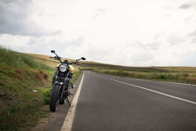 Motorcycle on country road amidst field against sky