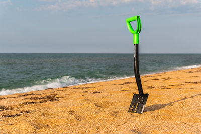 Hiking shovel in the sand, with a bright green handle so as not to lose it. sea beach, hiking camp