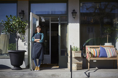 Full length portrait of female owner standing by doorway at store