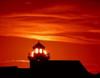 Silhouette building by sea against orange sky