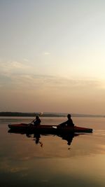 Silhouette men on boat in sea against sky during sunset