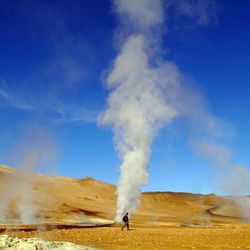 Man walking by hot spring against blue sky on sunny day