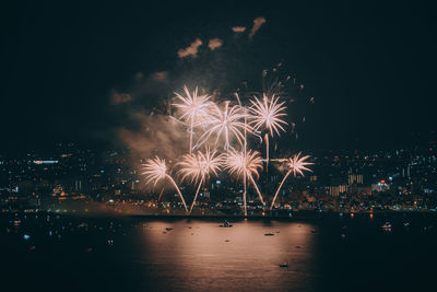 Firework display over illuminated city against sky at night