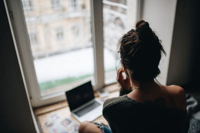 Rear view of woman using mobile phone at home