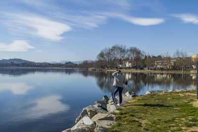 Rear view of man standing by lake against sky