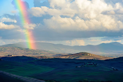 Scenic view of rainbow over mountains against cloudy sky