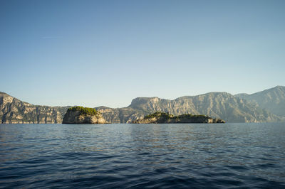 Scenic view of sea and mountains against clear blue sky