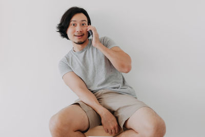 Portrait of smiling man talking on phone while sitting against wall