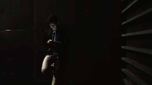 Full length of man using phone while standing in dark room