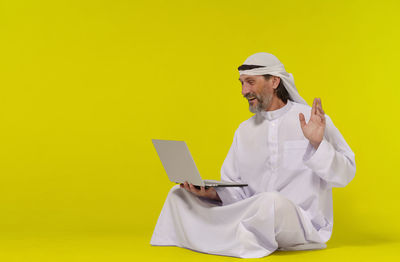 Rear view of female doctor using mobile phone against yellow background