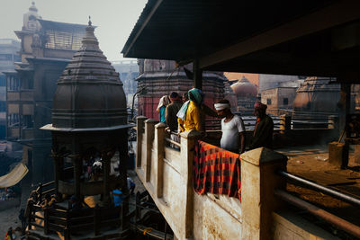 Varanasi, india - february, 2018: locals standing on balcony of city construction in old holy town with ancient buildings and temples
