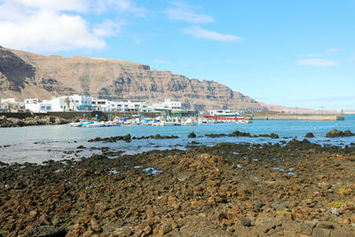 Rocky beach with orzola village and harbor on the background in lanzarote, canary islands, spain