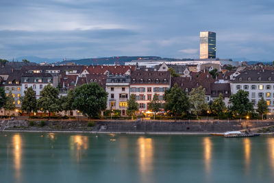 Buildings by river against sky in city at dusk