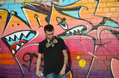 Full length of young man standing against graffiti wall