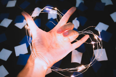 Cropped hand of person holding illuminated lighting equipment in heart shape at home