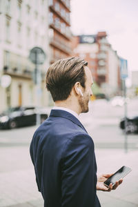 Side view of businessman talking through headphones in city