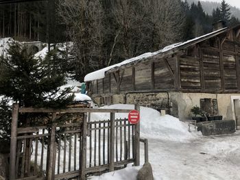 Snow covered field by trees and houses against mountain