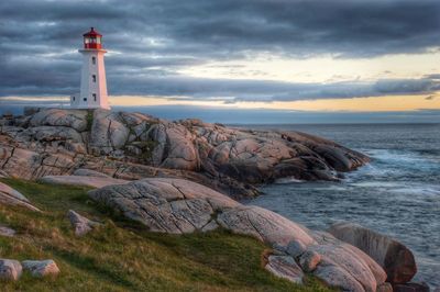 Lighthouse on rock formation by sea against sky during sunset