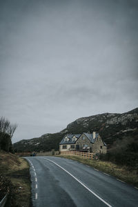 Country road leading towards mountain against sky