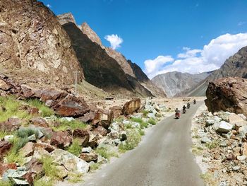 Bikers on road by mountains against sky