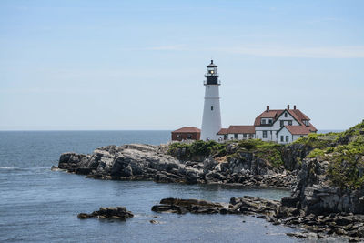 Lighthouse amidst sea and buildings against sky