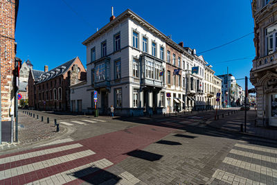 Road by buildings in city against clear blue sky