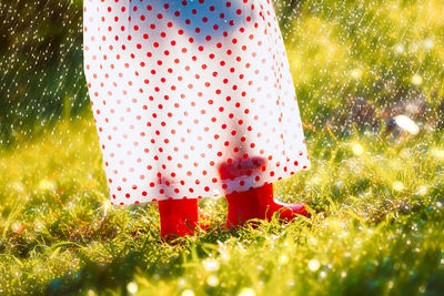 Low section of person wearing rubber boots and raincoat while standing on grass during rainfall