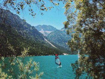Man windsurfing on lake by mountains