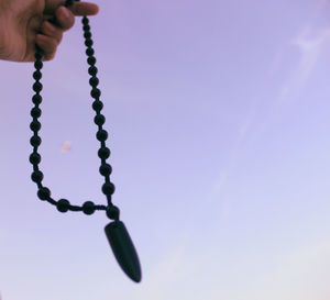 Low angle view of hand holding hanging against sky