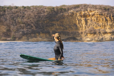 Happy woman sitting on surfboard in sea