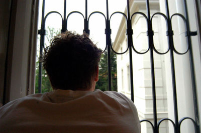 Rear view of man looking through window at home