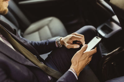 Midsection of businessman using device screen while sitting in car