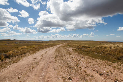Dirt road amidst field against sky