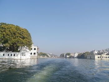 Buildings by sea against clear blue sky