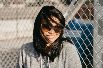 Portrait of smiling young woman standing by chainlink fence