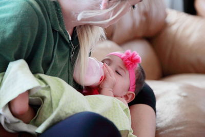 Close-up of mother feeding baby with milk bottle on sofa