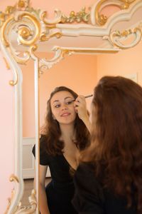 Beautiful woman applying eyeliner reflecting on mirror at home