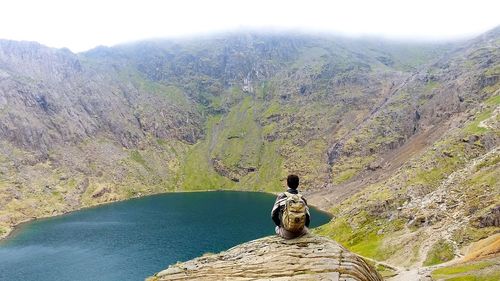 Rear view of people sitting on rock by mountain