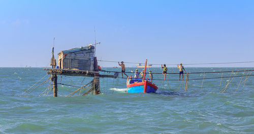 People on boat in sea against clear blue sky