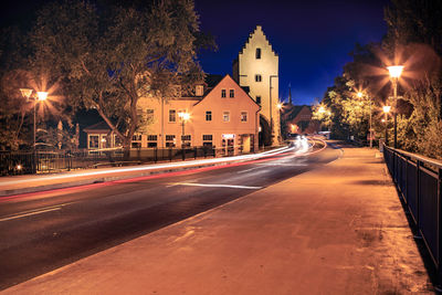 Light trails on road by buildings at night