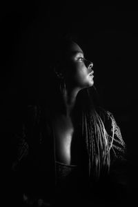 Side view of young woman standing against black background