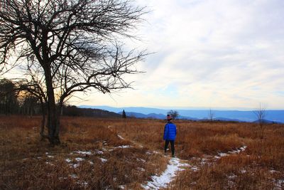 Rear view of man standing on field against sky