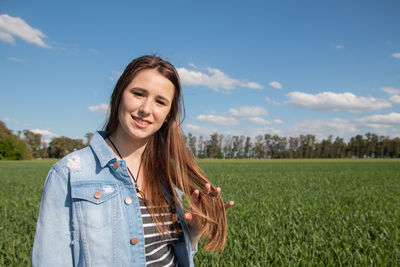 Portrait of young woman standing on field against sky