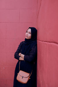 Portrait of young woman standing against wall