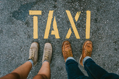 Low section of people wearing shoes while standing on road sign